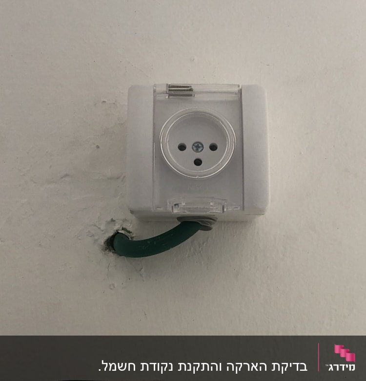 שקע חשמלי עם כבל ירוק בקיר לבן